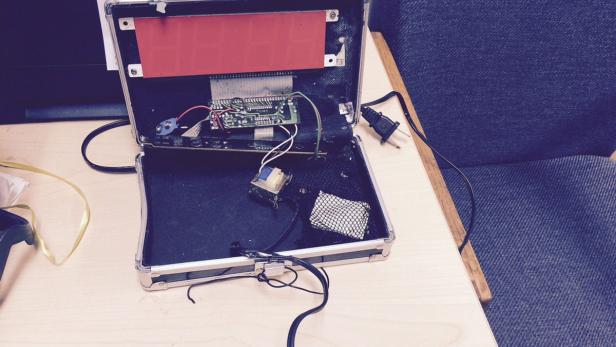 Ein geöffneter Koffer mit Elektronikbauteilen und einem roten Display liegt auf einem Tisch.
