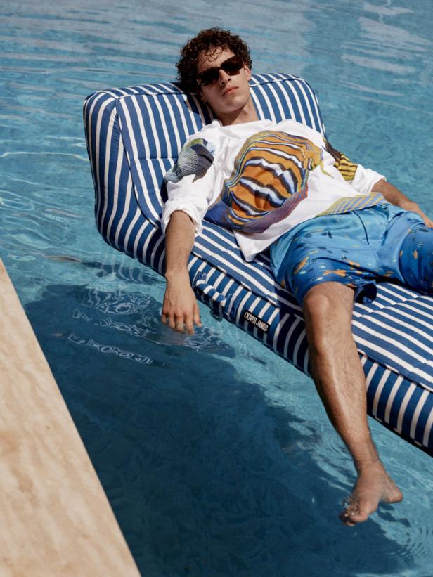 Ein Mann mit Sonnenbrille liegt auf einer blau-weiß gestreiften Luftmatratze im Pool.