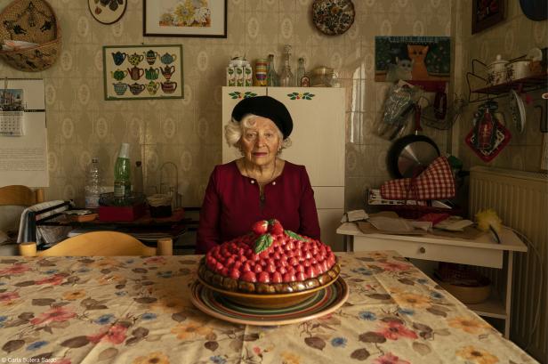 Eine ältere Frau sitzt an einem Tisch mit einem großen Erdbeerkuchen.
