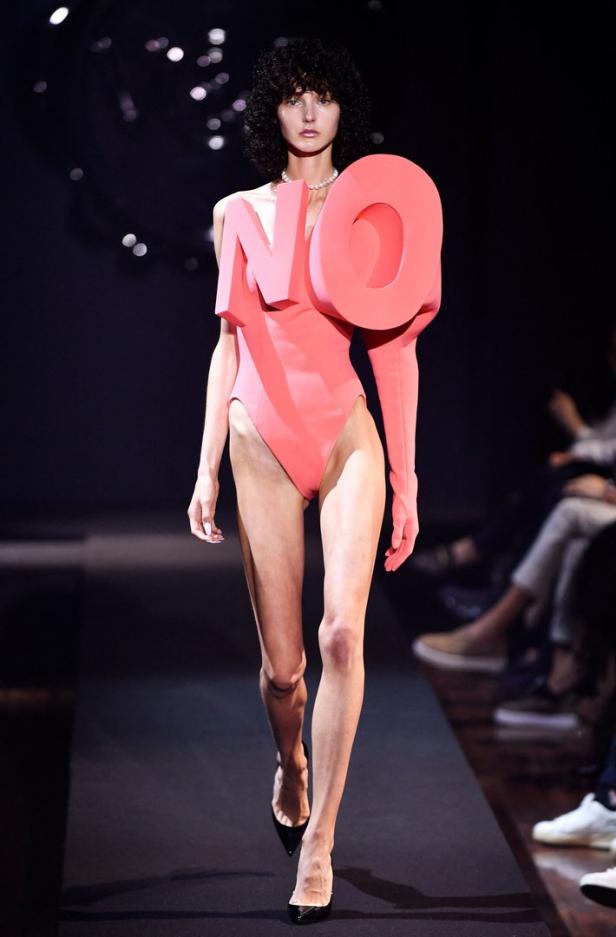 Ein Model mit einem korallfarbenen Body mit der aufgesetzten Aufschrift „NO“ auf dem Laufsteg.