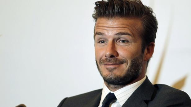 David Beckham in einem dunklen Anzug vor einem weißen Hintergrund.