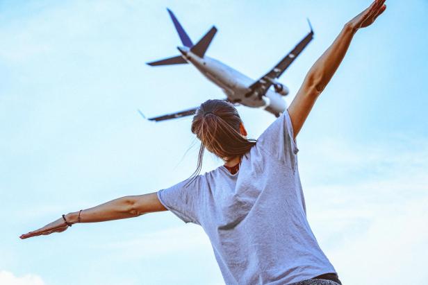 Rear view of a young woman with outstretched arms imitating flying commercial airplane above her