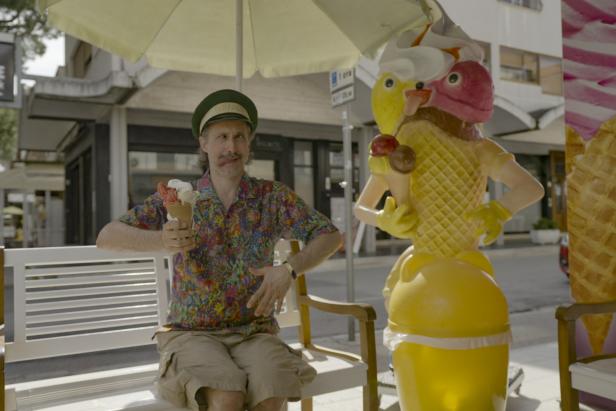 Ein Mann mit Eis sitzt neben einer skurrilen Eisdielen-Figur.