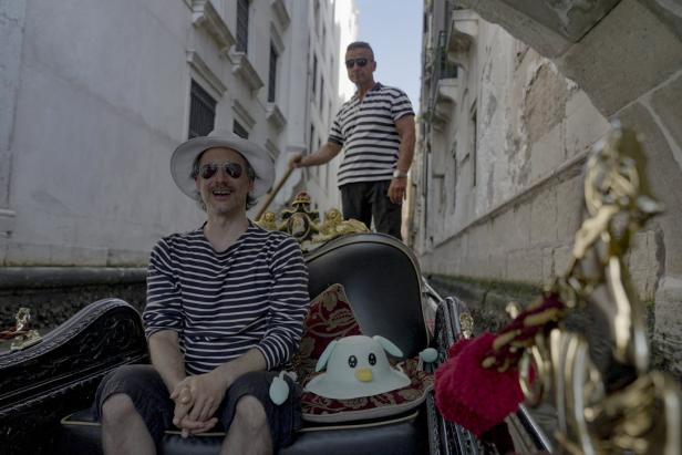 Ein Mann mit Hut und Sonnenbrille fährt in einer Gondel durch Venedig.