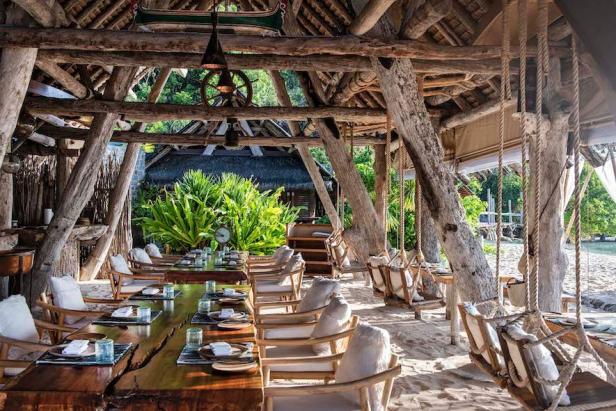 Die „Boat House Bar“ im Bawah Reserve mit Tischen und Schaukeln am Strand.