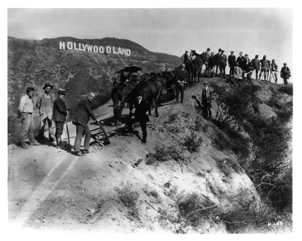 Eine Gruppe von Männern und ein von Pferden gezogener Wagen vor dem „Hollywoodland“-Schriftzug.