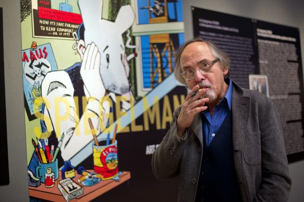 Art Spiegelman mit einer Zigarette vor einem Ausstellungsplakat von „Maus“.