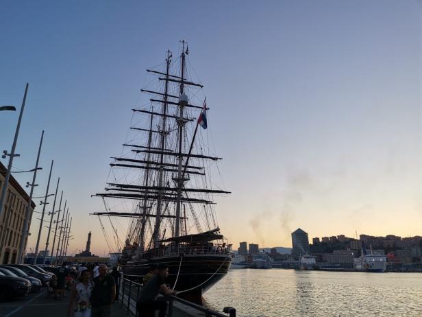 Ein großes Segelschiff liegt im Hafen vor der Skyline von Genua.