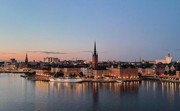 Blick auf Stockholm bei Dämmerung mit Riddarholmskirche und Schiffen am Ufer.