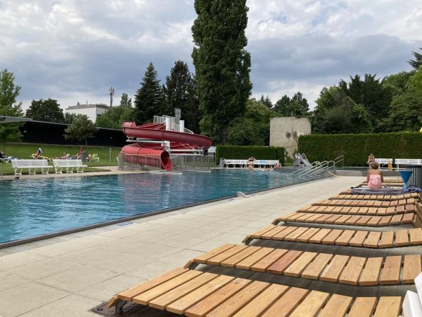 Ein Freibad mit Schwimmbecken, Liegestühlen und einer roten Wasserrutsche.