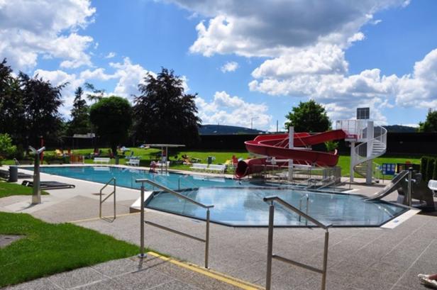 Ein Freibad mit roter Wasserrutsche und Liegewiese unter blauem Himmel.