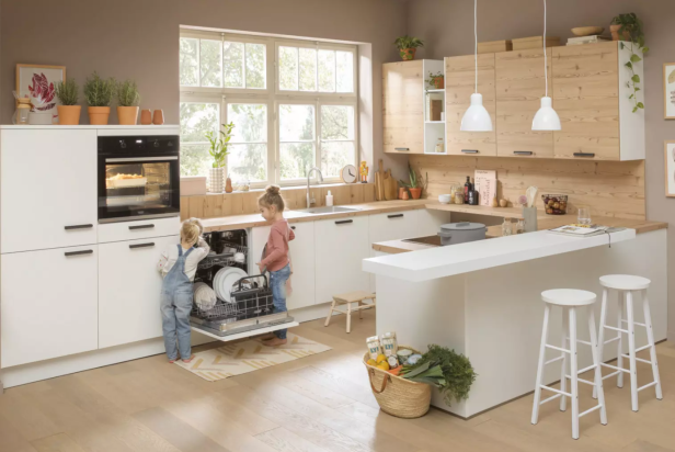 Zwei Kinder räumen in einer hellen, modernen Küche gemeinsam einen Geschirrspüler aus.