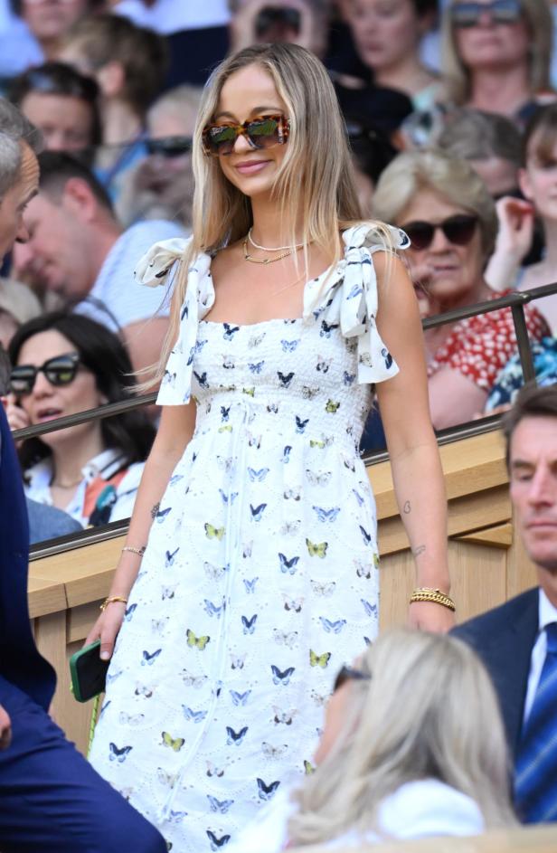 Eine Frau mit Sonnenbrille und einem Kleid mit Schmetterlingsmuster sitzt im Publikum.