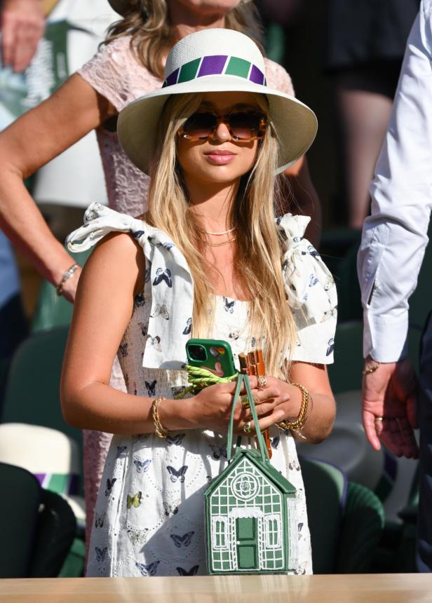 Eine Frau mit Hut und Sonnenbrille hält eine grüne Handtasche in Form eines Gewächshauses.