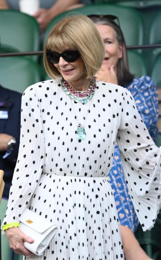 Anna Wintour mit Sonnenbrille und gepunktetem Kleid bei einem Tennismatch.