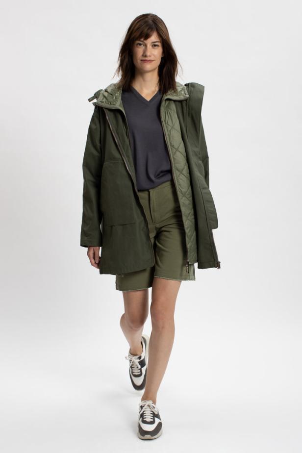 Eine Frau in einem olivgrünen Outfit mit Jacke und Shorts, dazu passende Turnschuhe.