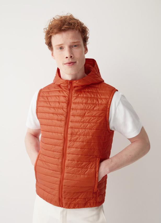 Ein Mann mit roten Haaren trägt eine orangefarbene Steppweste mit Kapuze.