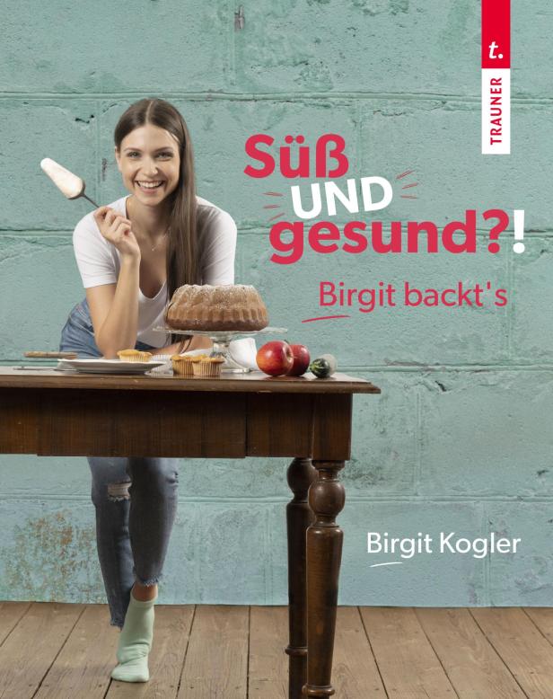 Eine lächelnde Frau präsentiert einen Kuchen und andere Backwaren auf einem Tisch.