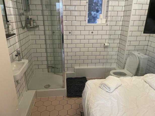 Ein Badezimmer mit Dusche, Waschbecken, Toilette und einem Bett.