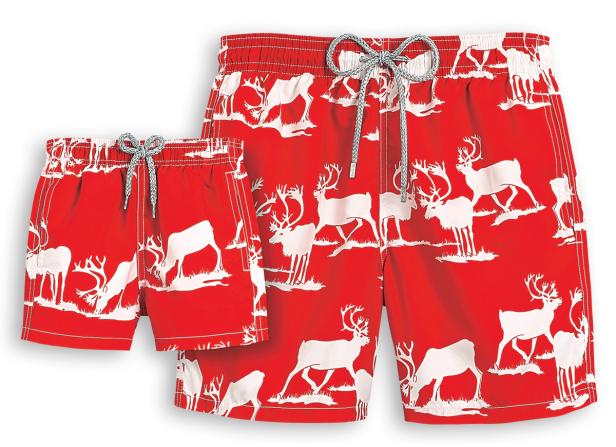 Eine rote Badehose für Erwachsene und eine passende für Kinder mit einem weißen Rentier-Muster.