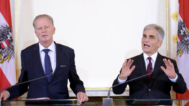 Zwei Männer in Anzügen stehen vor österreichischen Flaggen und sprechen.