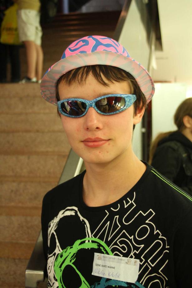 Ein Jugendlicher mit Hut und glitzernder Sonnenbrille blickt in die Kamera.