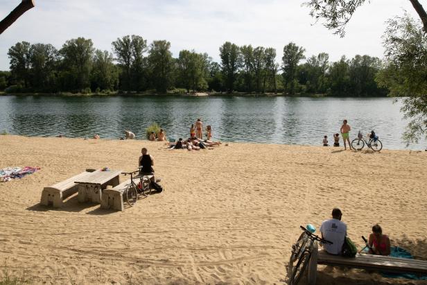 An einem sonnigen Tag entspannen sich Menschen an einem Sandstrand an einem See.