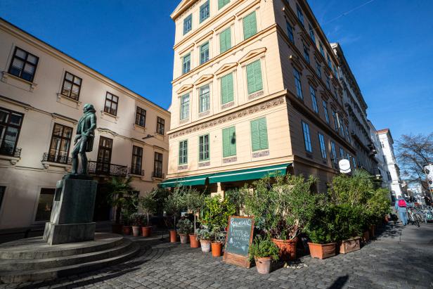 Eine Statue vor einem Café in einer Wiener Stadtlandschaft.