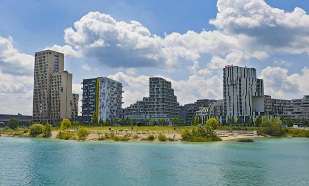 Moderne Wohngebäude am Ufer eines Sees unter einem bewölkten Himmel.