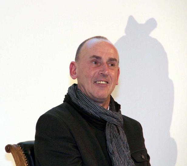 Ein Mann mit Schal und dunkler Jacke lächelt.