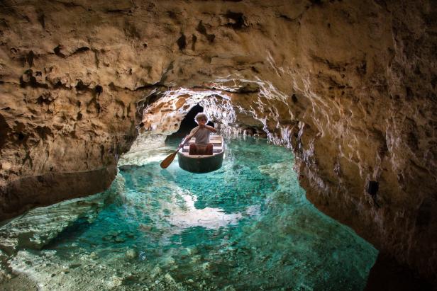 Ein Mann paddelt mit einem Kanu durch eine unterirdische Höhle mit klarem, türkisfarbenem Wasser.