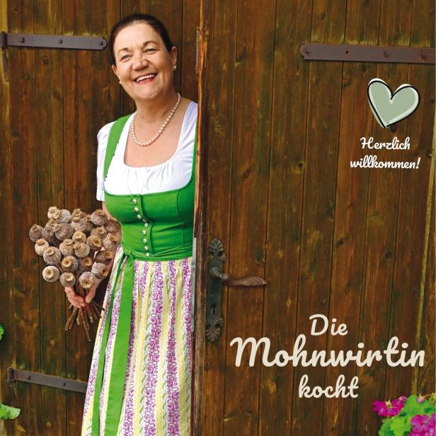 Eine lächelnde Frau im Dirndl steht in einer Holztür und hält einen Mohnblumenstrauß.