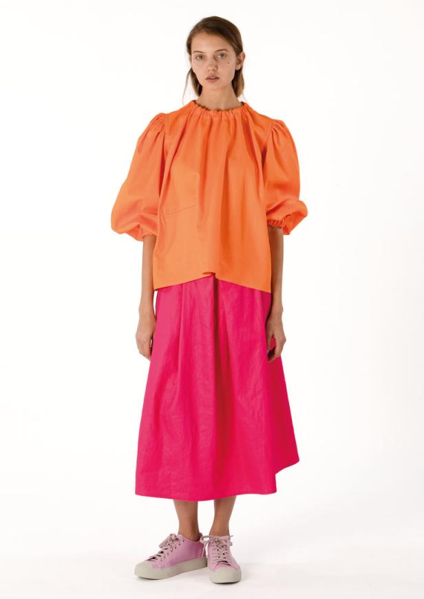 Eine Frau trägt eine orangefarbene Bluse und einen pinkfarbenen Rock.
