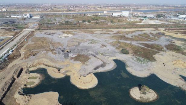 Luftaufnahme einer Baustelle mit einem See und einem kleinen Bagger.