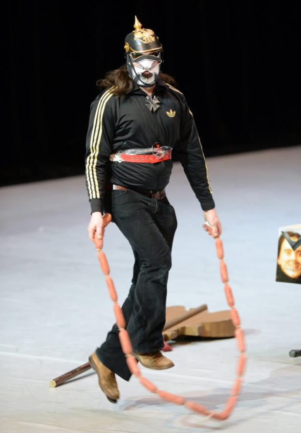 Ein Mann mit Pickelhaube und Maske springt Seil mit einer Wurstkette.