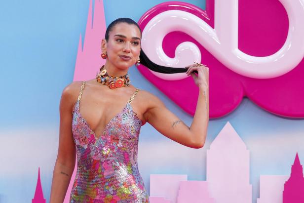 Dua Lipa posiert in einem bunten Kleid auf einem pinkfarbenen Teppich.