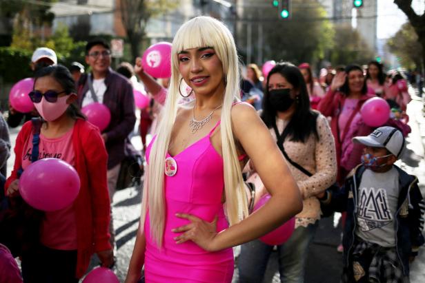 Eine Frau in einem pinkfarbenen Kleid und blonder Perücke bei einer Kundgebung mit pinkfarbenen Ballons.