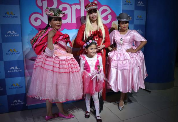 Drei Frauen und ein Mädchen posieren in traditionellen Kleidern vor einem „Barbie“-Hintergrund.