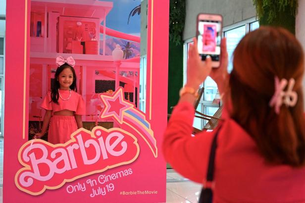 Ein Mädchen posiert vor einem „Barbie“-Filmplakat, während eine Person ein Foto macht.