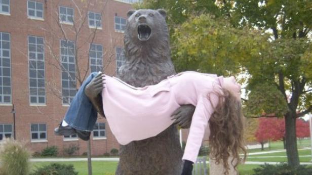 Eine Frau wird von einer Bärenstatue im Arm gehalten.