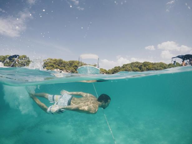 Ein Mann schwimmt im türkisfarbenen Wasser vor Menorca.