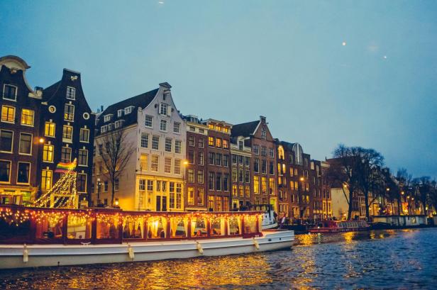 Ein beleuchtetes Boot fährt auf einem Kanal in Amsterdam entlang historischer Gebäude.