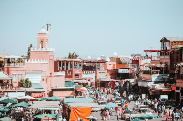 Blick auf den belebten Marktplatz von Marrakesch mit Menschen, Ständen und Gebäuden.