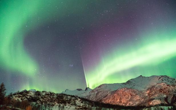 Grüne und violette Polarlichter über einer verschneiten Berglandschaft.