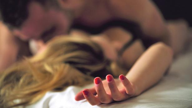 Ein Paar liegt zusammen im Bett, der Fokus liegt auf der Hand der Frau mit rotem Nagellack.