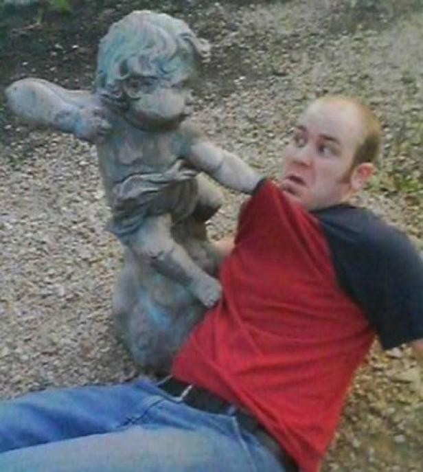 Ein Mann erschrickt, als eine Amorstatue an seinem Hemd zieht.