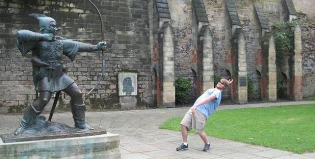 Ein Mann posiert, als würde er von einer Robin-Hood-Statue beschossen werden.