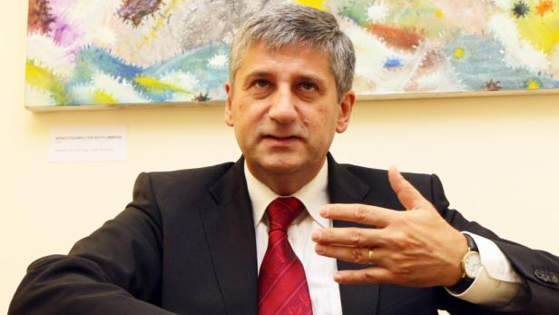 Ein Mann im Anzug gestikuliert vor einem abstrakten Gemälde.