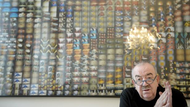 Ein Mann mit Brille sitzt vor einem großen Bild mit vielen kleinen Abbildungen.