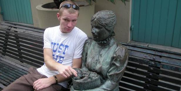 Ein Mann sitzt neben einer Bronzestatue auf einer Bank.